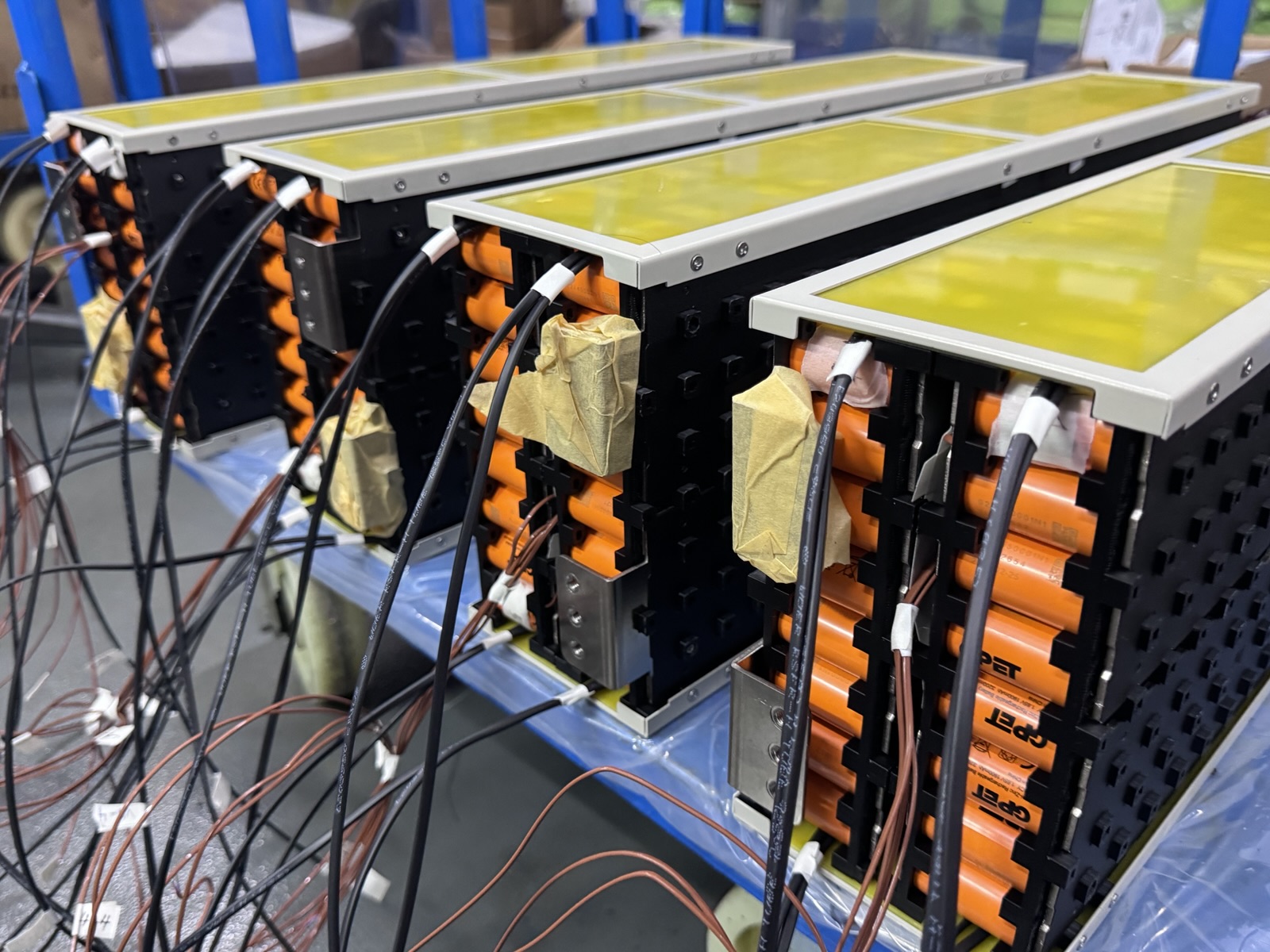 Rows of battery packs built from orange cylindrical cells, wired up for testing in the GP factory